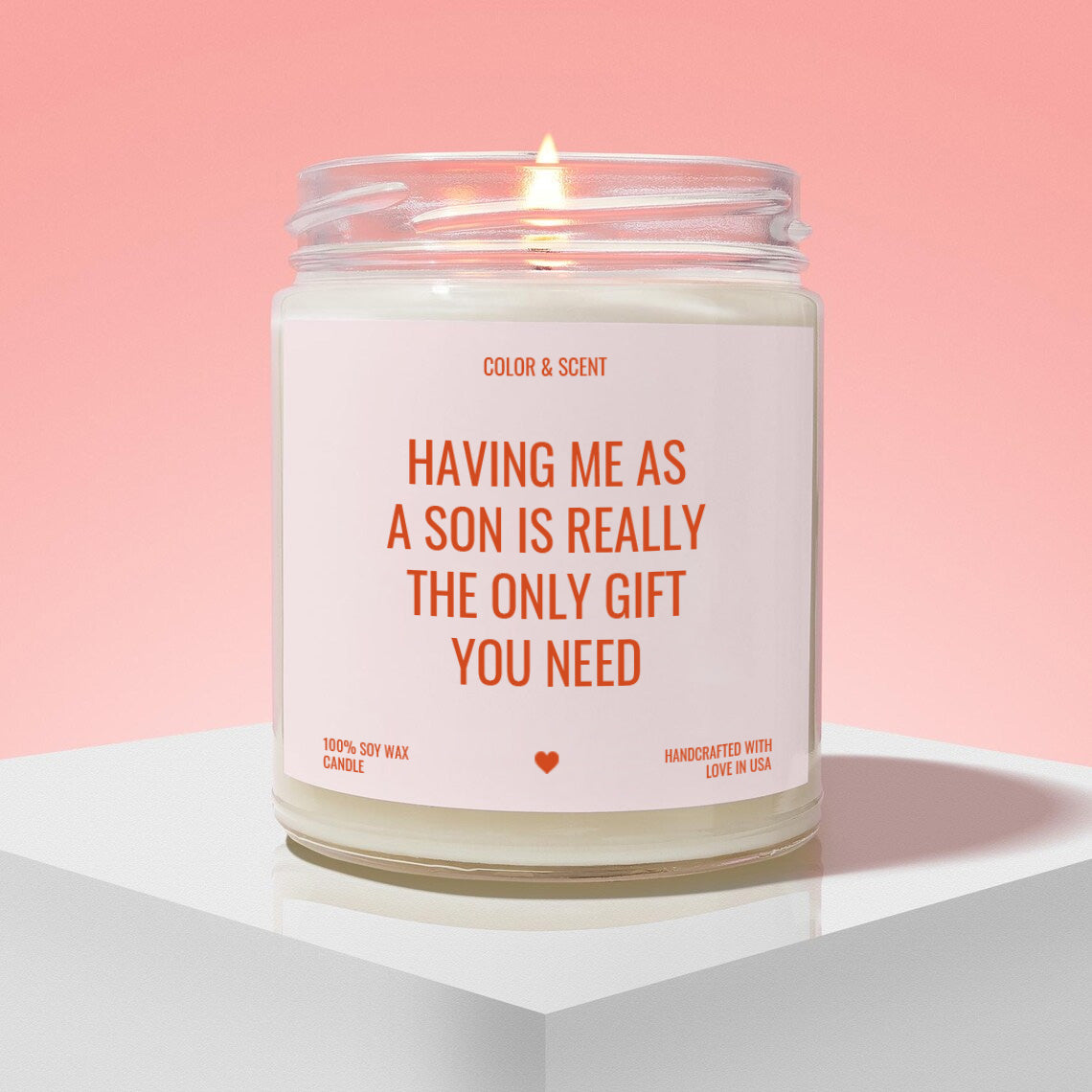 a candle labeled "Having Me as a Son is Really the Only Gift You Need" against a pink background.