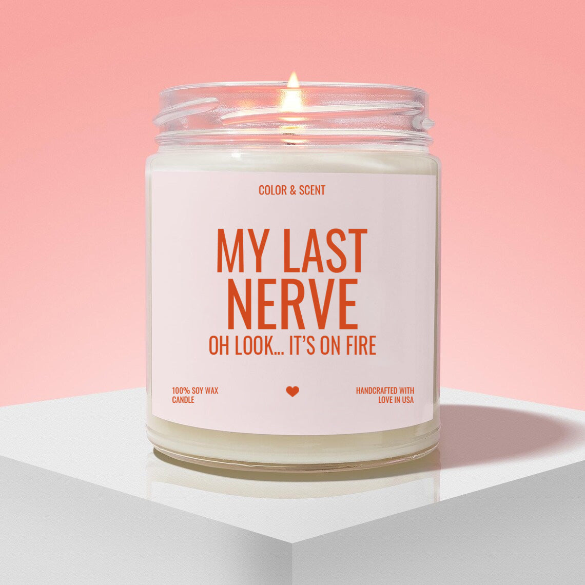 a candle labeled "My Last Nerve" with a flame, placed on a white pedestal against a pink background.