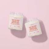 Two white candles with orange text labels are placed on a pink background.