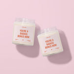 Two white candles with orange text labels are placed on a pink background.