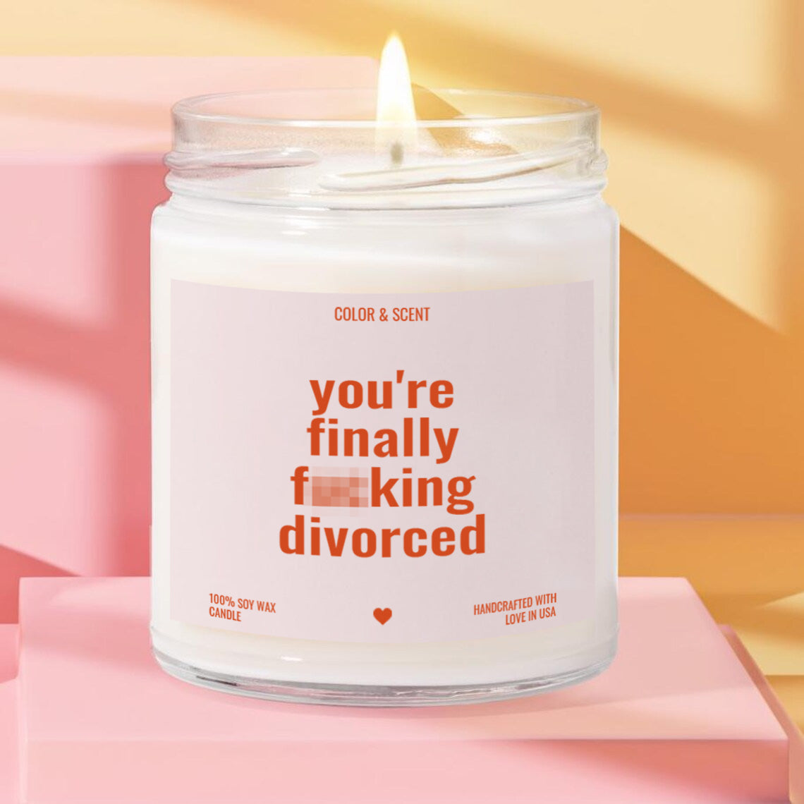 A white candle with a lit flame, featuring a humorous text label that reads "you're finally fucking divorced".