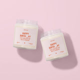 Two white candles with orange labels are placed on a pink background.