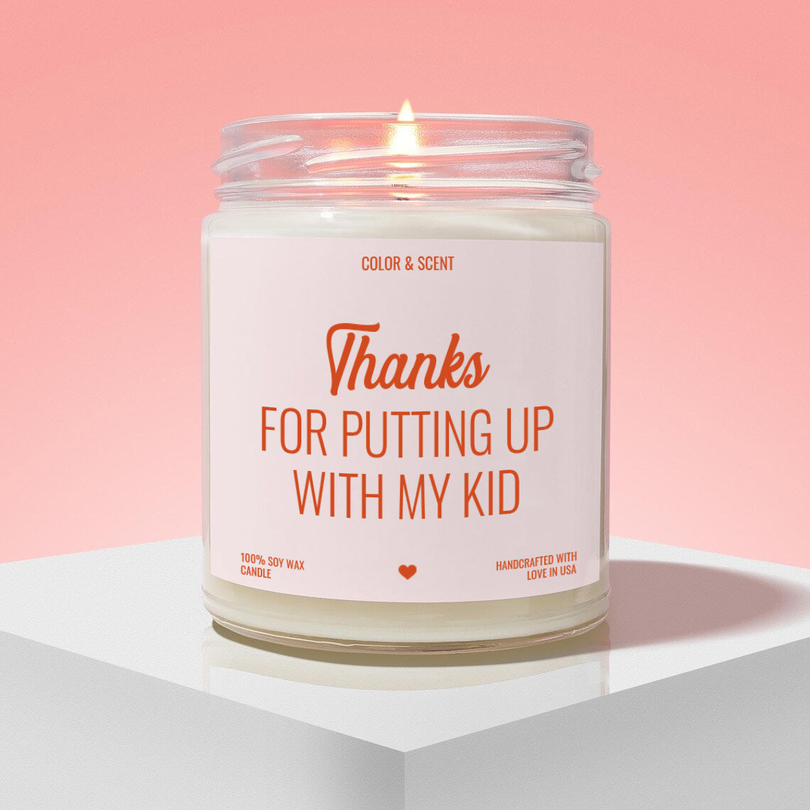 A white candle with a lit flame, labeled as a "Thanks for putting up with my kid" candle.